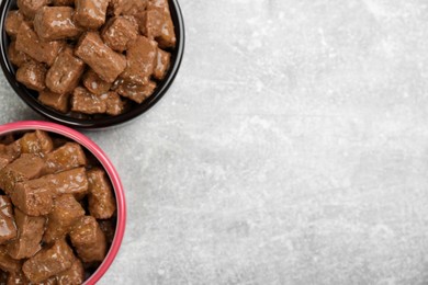 Wet pet food in feeding bowls on light grey background, flat lay. Space for text