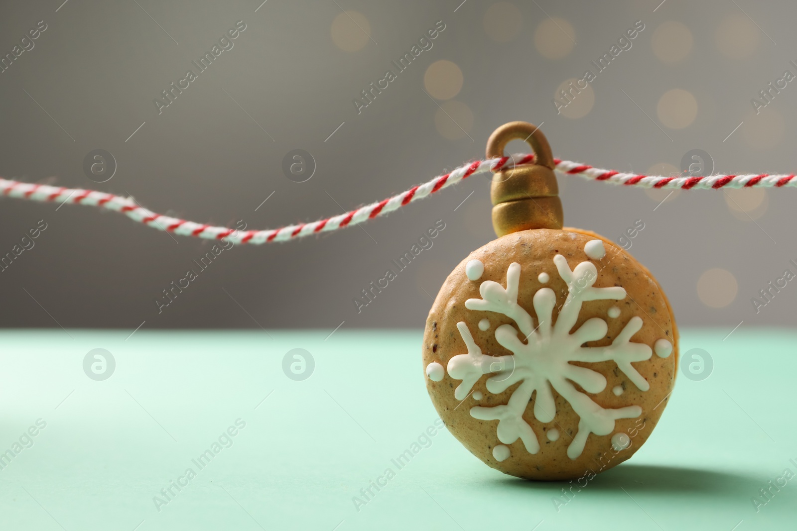 Photo of Beautifully decorated Christmas macaron with rope on turquoise table against blurred festive lights