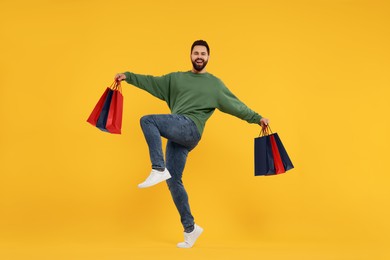 Photo of Smiling man with many paper shopping bags dancing on orange background