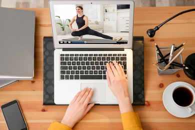 Image of Woman watching morning exercise video on laptop at table, top view