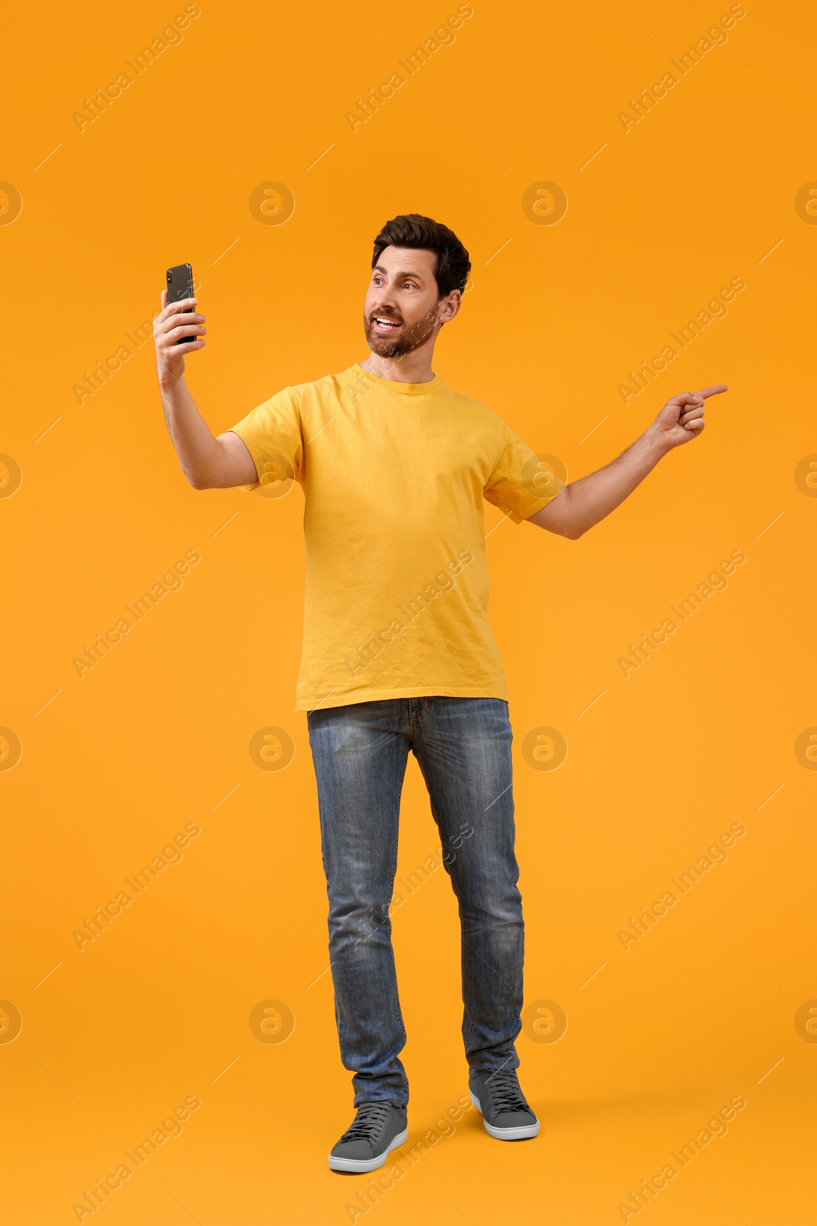 Photo of Smiling man taking selfie with smartphone on yellow background