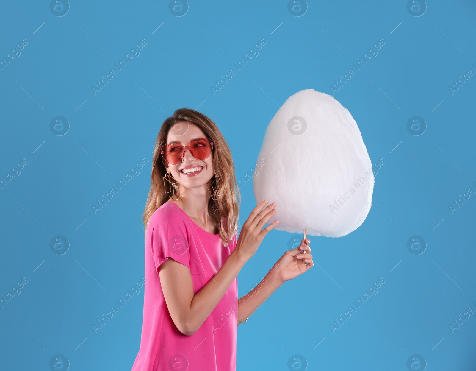 Photo of Happy young woman with cotton candy on blue background