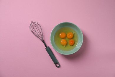 Photo of Metal whisk and raw eggs in bowl on pink background, flat lay