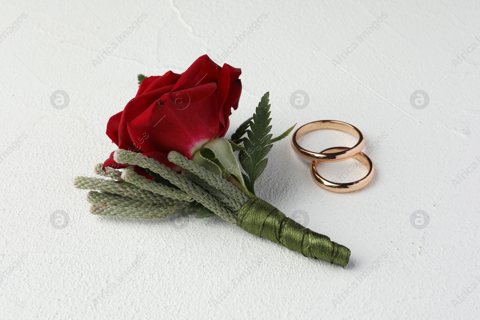 Photo of Stylish red boutonniere and rings on white textured table
