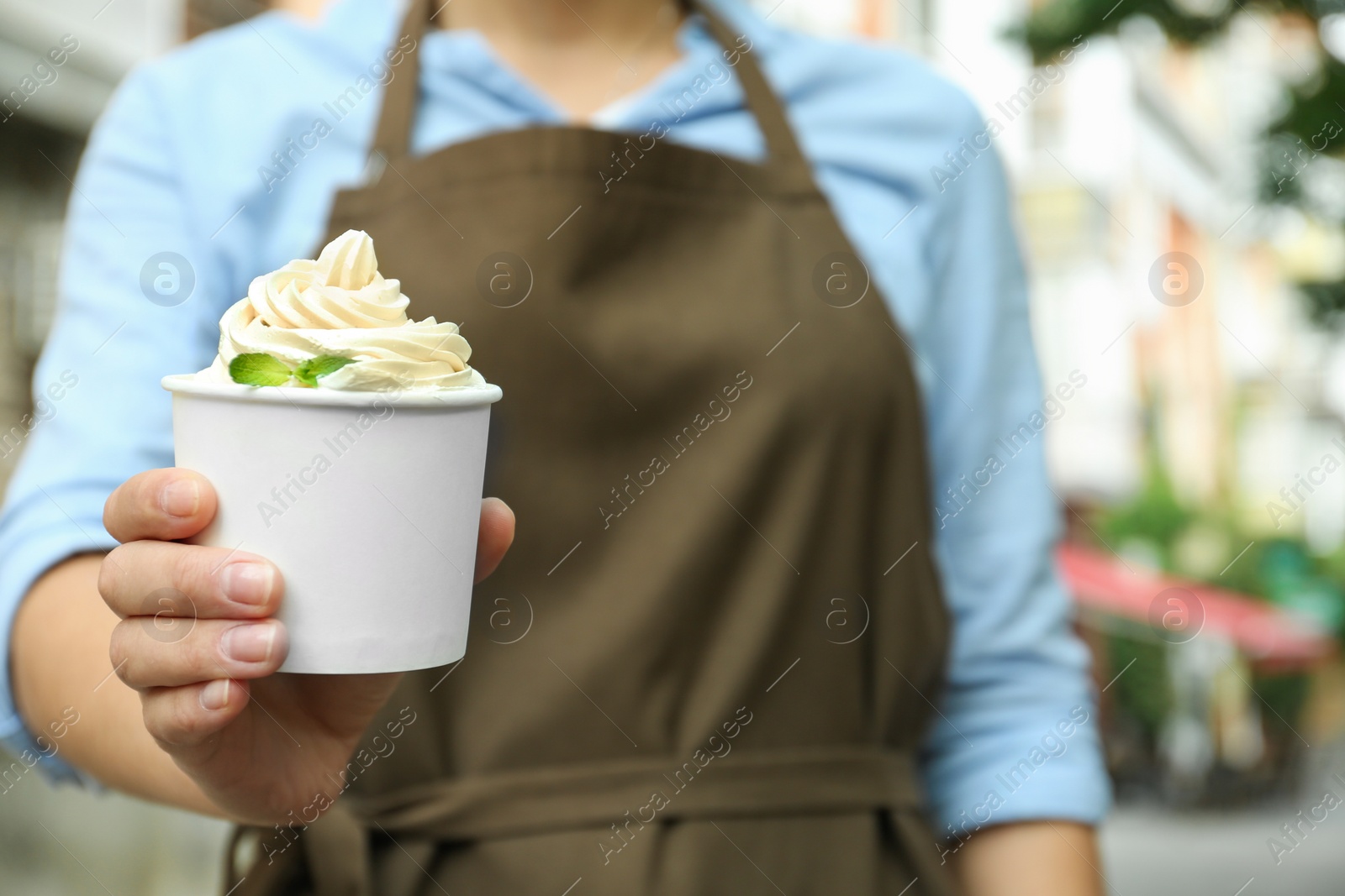 Photo of Woman holding cup with tasty frozen yogurt outdoors, closeup