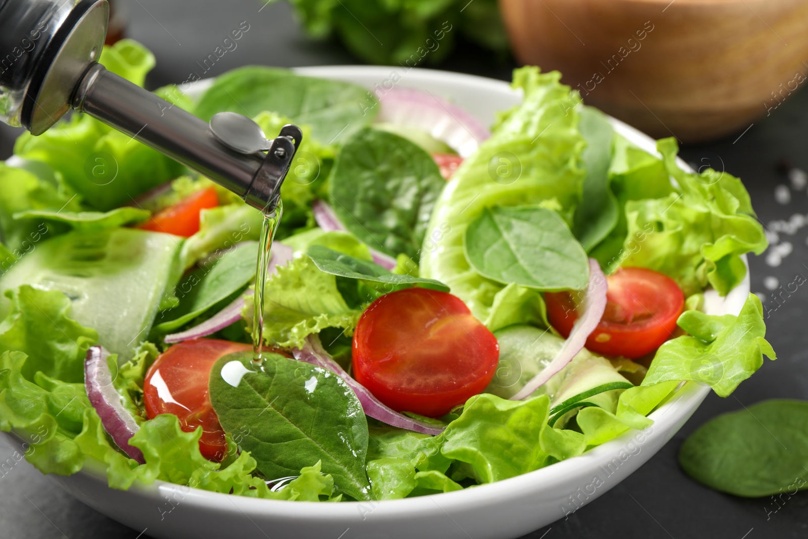 Photo of Pouring oil into delicious vegetable salad on table, closeup