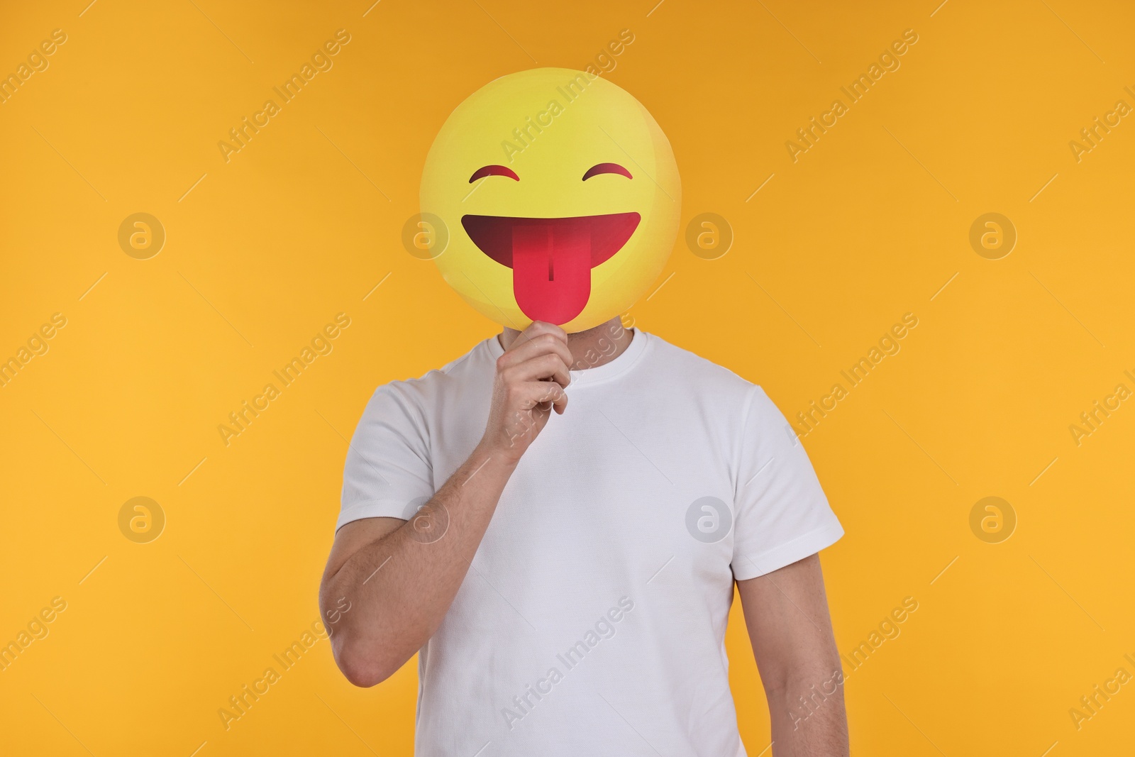 Photo of Man covering face with emoticon sticking out tongue on yellow background