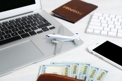 Smartphone with laptop, money and toy plane on light background. Travel agency