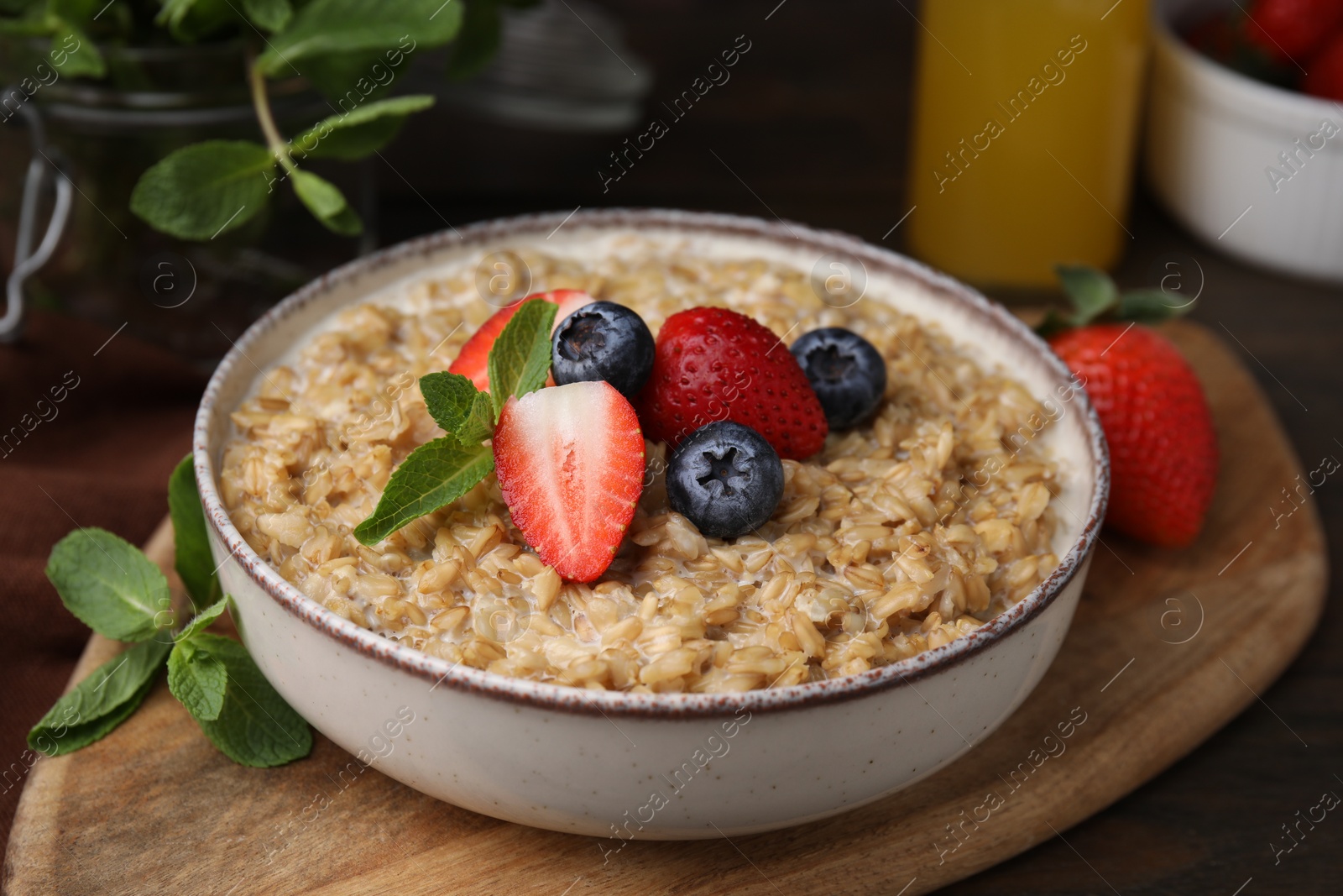 Photo of Tasty oatmeal with strawberries and blueberries in bowl on wooden table