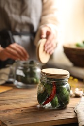 Photo of Woman pickling vegetables at table indoors, focus on jar with cucumbers