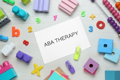 Photo of Flat lay composition with phrase ABA Therapy and colorful toys on white wooden table