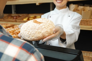 Baker giving customer fresh bread in store, closeup