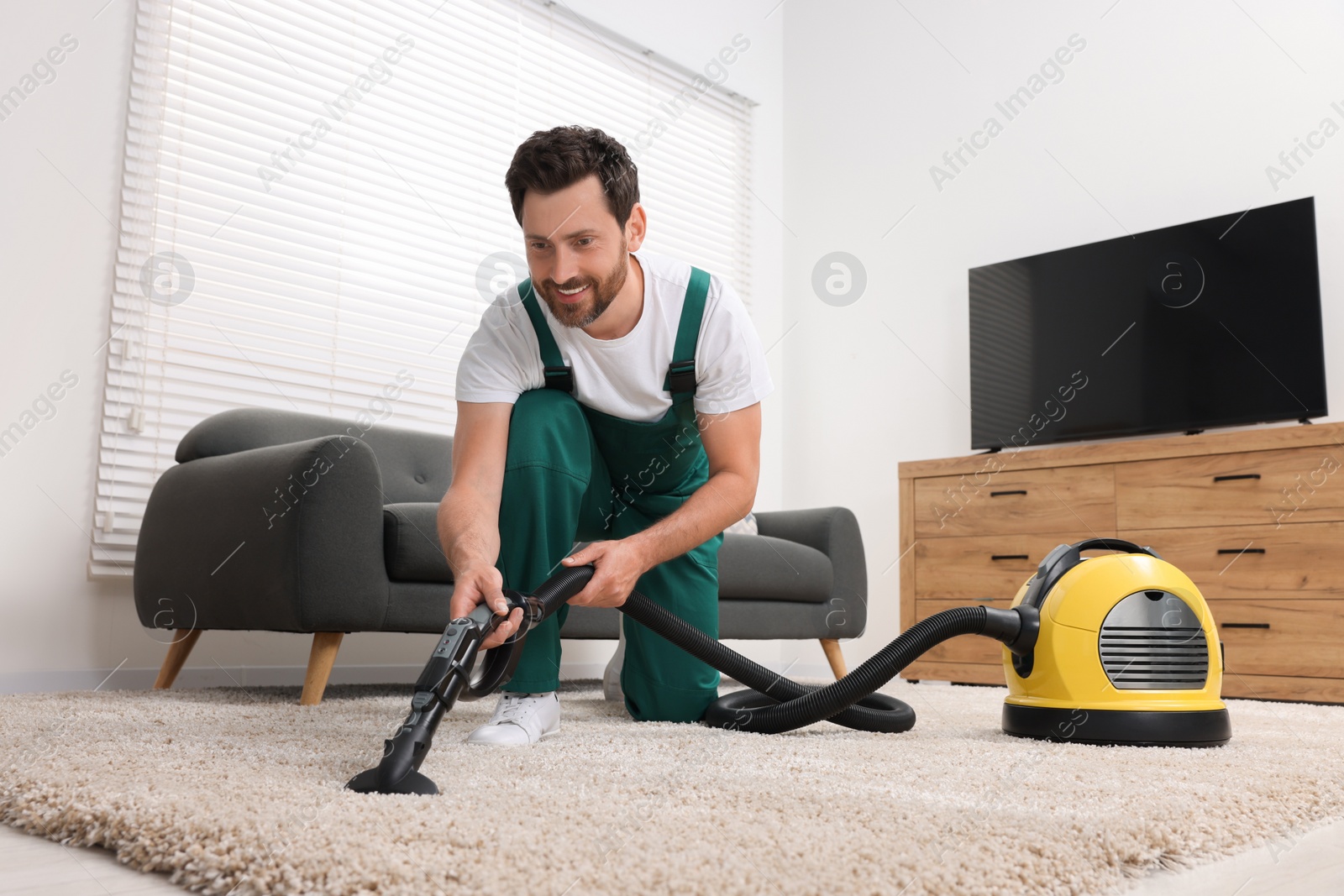 Photo of Dry cleaner's employee hoovering carpet with vacuum cleaner in room