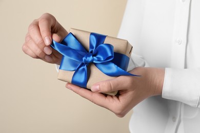Photo of Woman holding gift box with blue bow on beige background, closeup