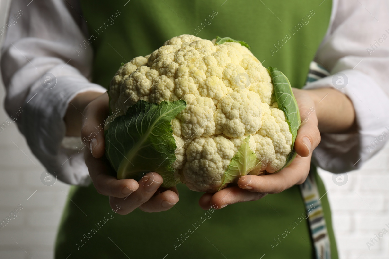 Photo of Woman holding fresh cauliflower against brick wall, closeup