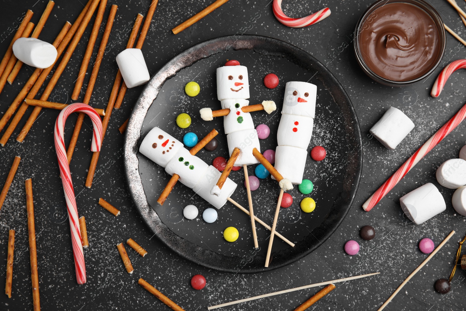 Photo of Flat lay composition with funny snowmen made of marshmallows on black table