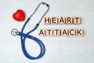 Photo of Wooden cubes with text Heart Attack and stethoscope on light background, flat lay
