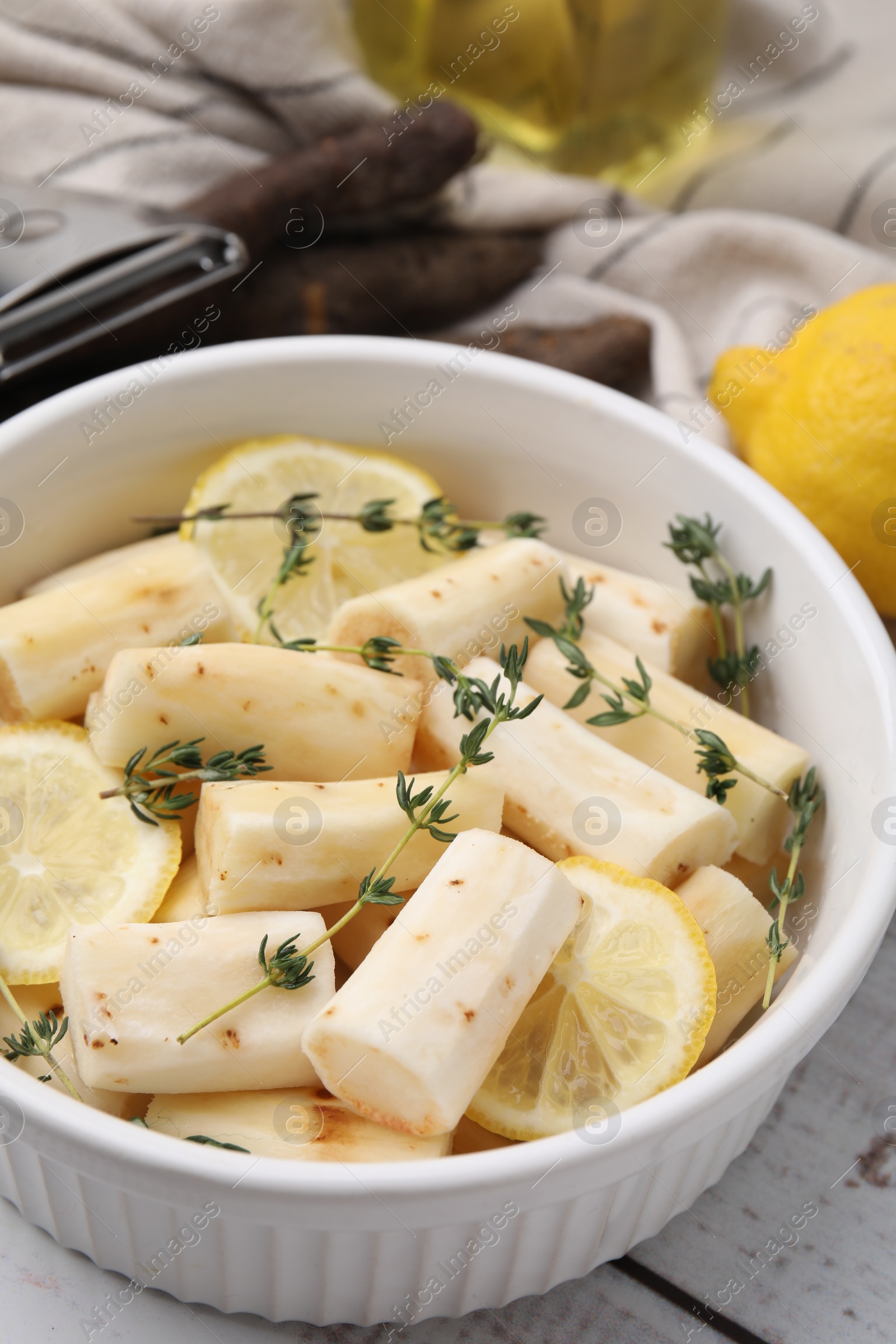 Photo of Dish with raw salsify roots, lemon and thyme on white wooden table, closeup