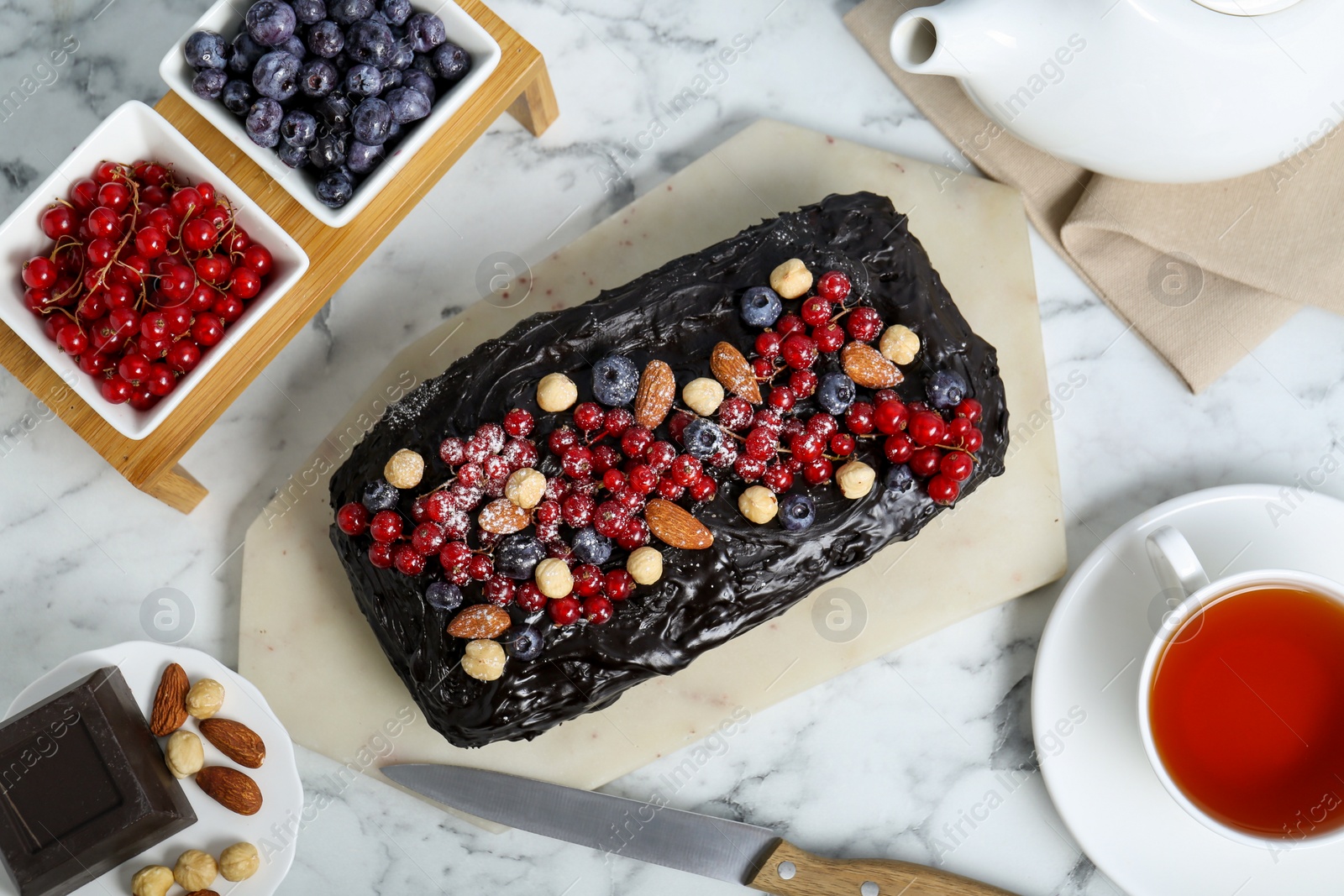 Photo of Delicious chocolate sponge cake, tea and ingredients on white marble table, flat lay