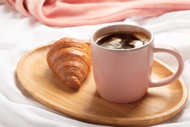 Wooden tray with cup of aromatic coffee and croissant on white fabric. Breakfast in bed