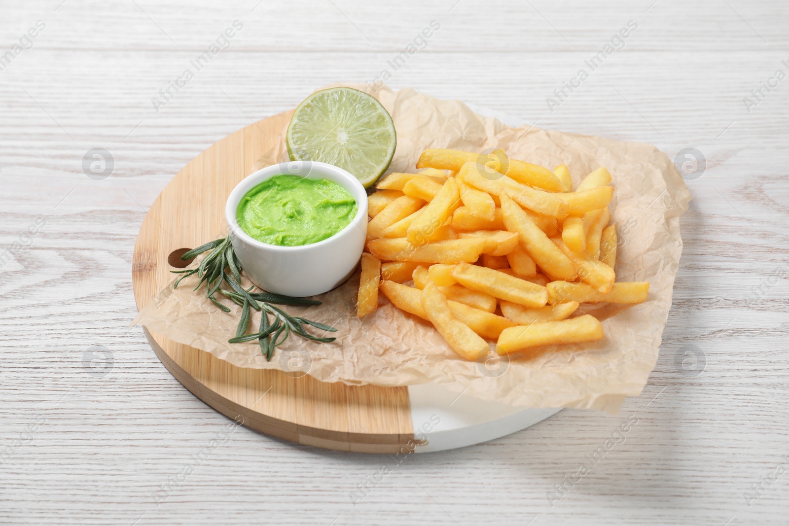 Photo of Delicious french fries, avocado dip, lime and rosemary served on white wooden table