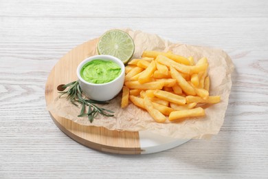 Photo of Delicious french fries, avocado dip, lime and rosemary served on white wooden table