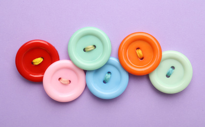 Photo of Many colorful sewing buttons on violet background, flat lay