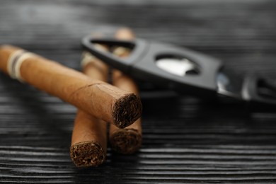 Cigars and guillotine cutter on black wooden table, closeup