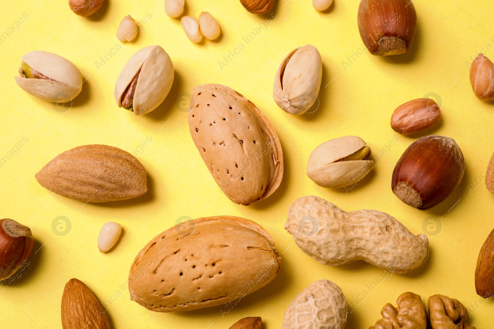 Photo of Different delicious nuts on yellow background, flat lay