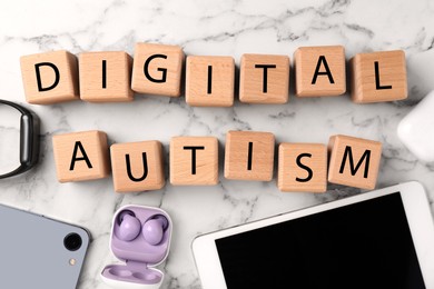 Photo of Phrase Digital Autism made of wooden cubes and devices on white marble table, flat lay. Addictive behavior