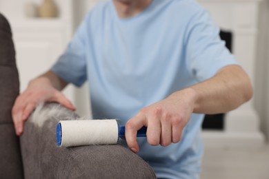 Pet shedding. Man with lint roller removing dog's hair from armchair at home, closeup