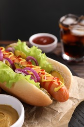 Photo of Delicious hot dog with lettuce, onion and pickle served on wooden table, closeup