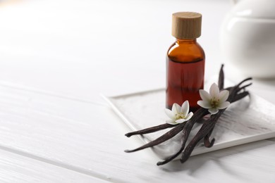 Photo of Vanilla pods, essential oil and flowers on white wooden table, space for text