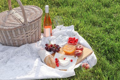 Photo of Picnic blanket with tasty food, basket and cider on green grass outdoors
