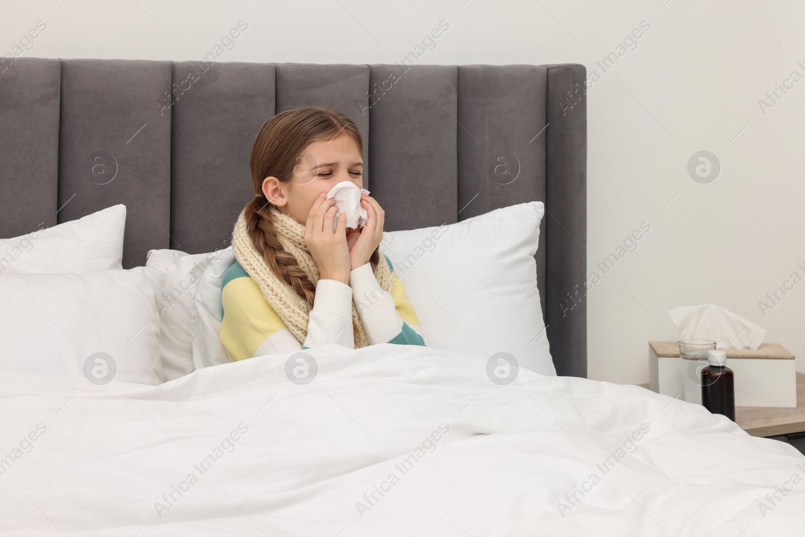 Photo of Sick girl with tissue coughing on bed at home