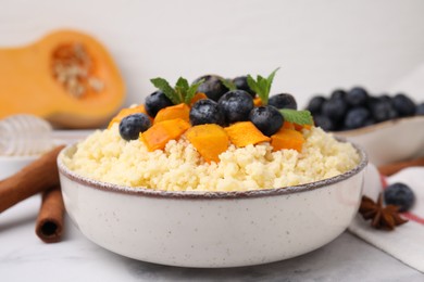 Photo of Bowl of tasty couscous with blueberries, pumpkin and mint on table, closeup