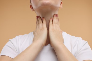 Woman touching her neck on beige background, closeup