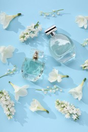 Luxury perfumes and floral decor on light blue background, flat lay