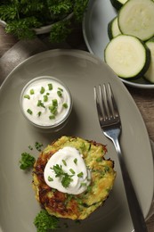 Photo of Delicious zucchini fritters with sour cream served on wooden table, flat lay