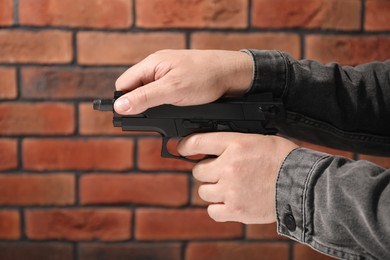 Dangerous criminal with gun near brick wall, closeup. Armed robbery