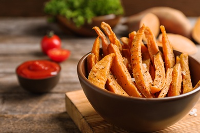 Bowl with sweet potato fries on wooden table, space for text