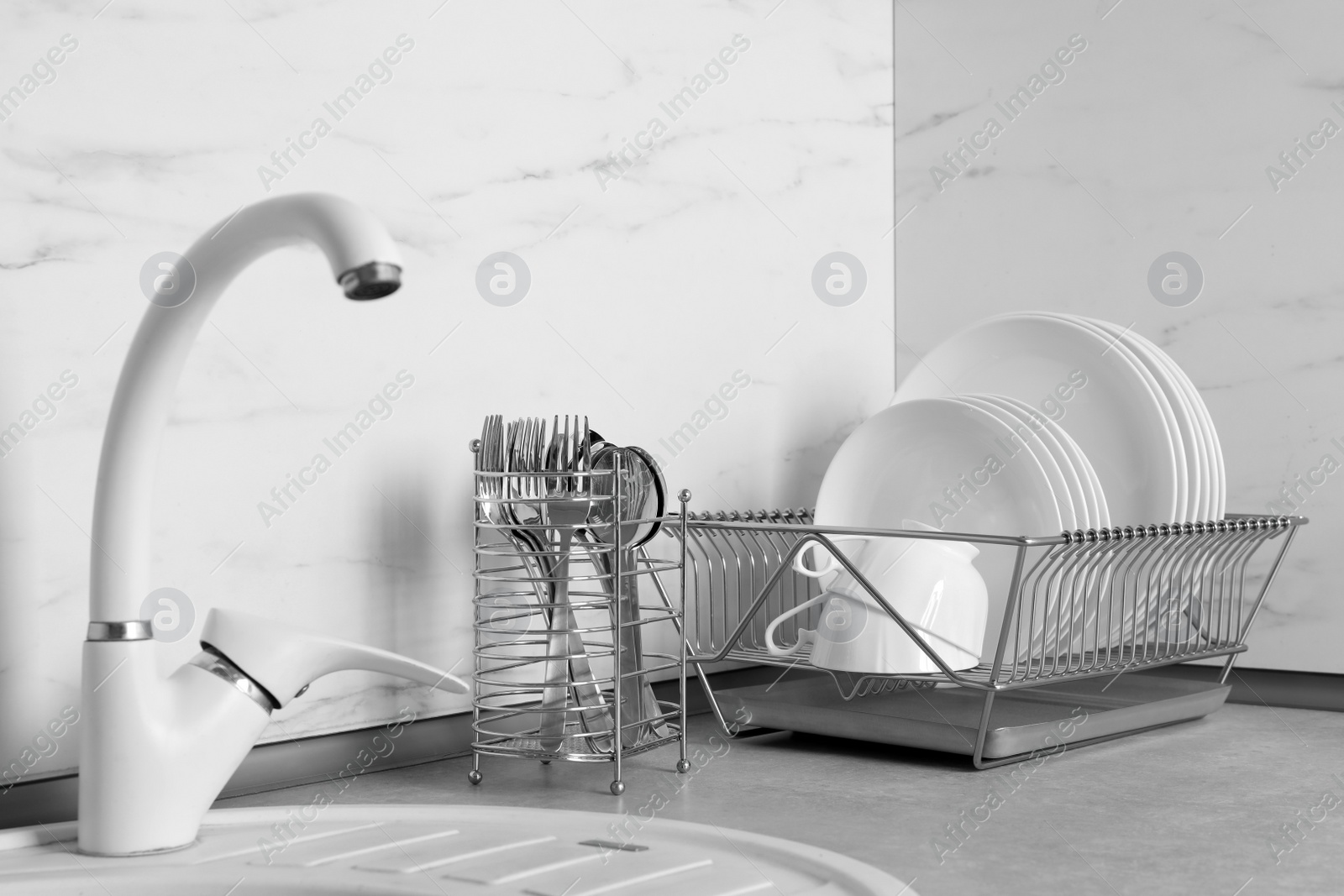 Photo of Drying rack with clean dishes and cutlery holder near sink in kitchen