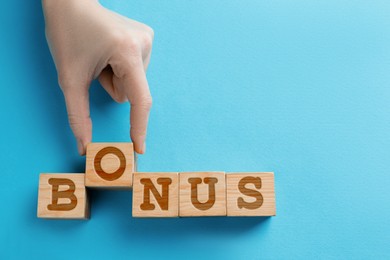 Woman making word Bonus of cubes with letters on light blue wooden background, top view. Space for text