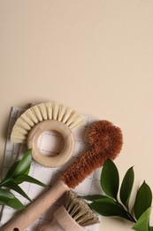 Photo of Cleaning brushes, towel and green leaves on beige background, top view. Space for text