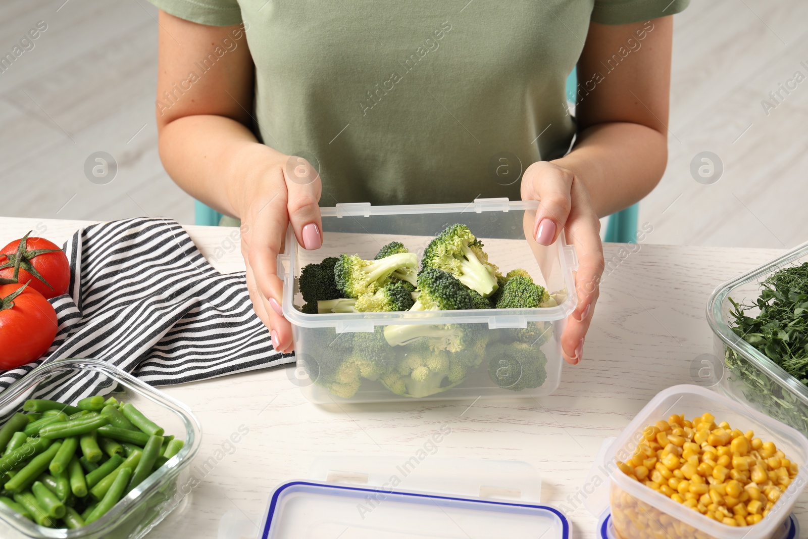 Photo of Woman holding plastic container with broccoli at white wooden table, closeup. Food storage