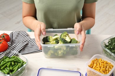 Photo of Woman holding plastic container with broccoli at white wooden table, closeup. Food storage