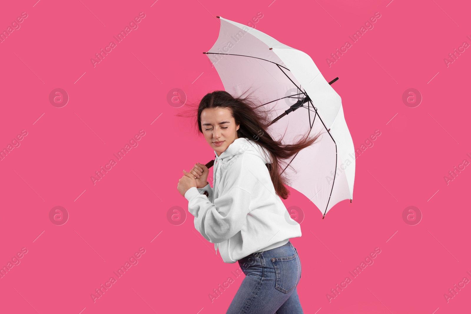 Photo of Woman with white umbrella caught in gust of wind on pink background