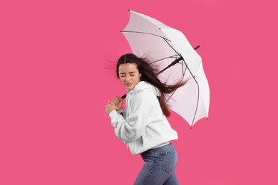 Woman with white umbrella caught in gust of wind on pink background