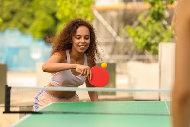 Photo of African-American woman playing ping pong with friend outdoors