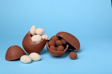Tasty broken chocolate eggs and sweets on light blue background